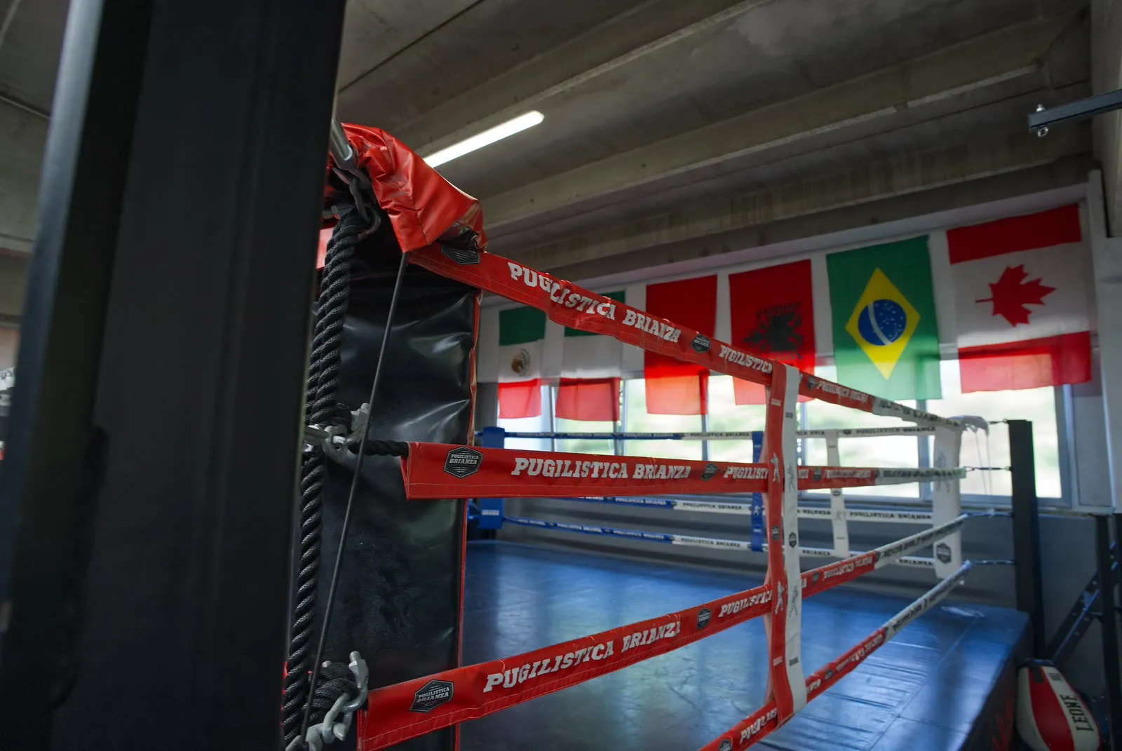 Vista panoramica della Pugilistica Brianza: sala sacchi pesanti e ring da boxe con bandiere internazionali