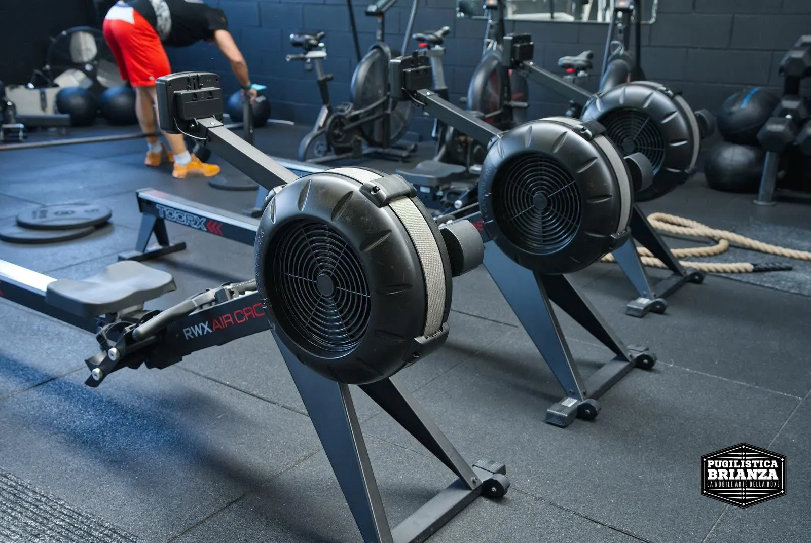 Rower nell'area Hyrox con atleta in allenamento sullo sfondo